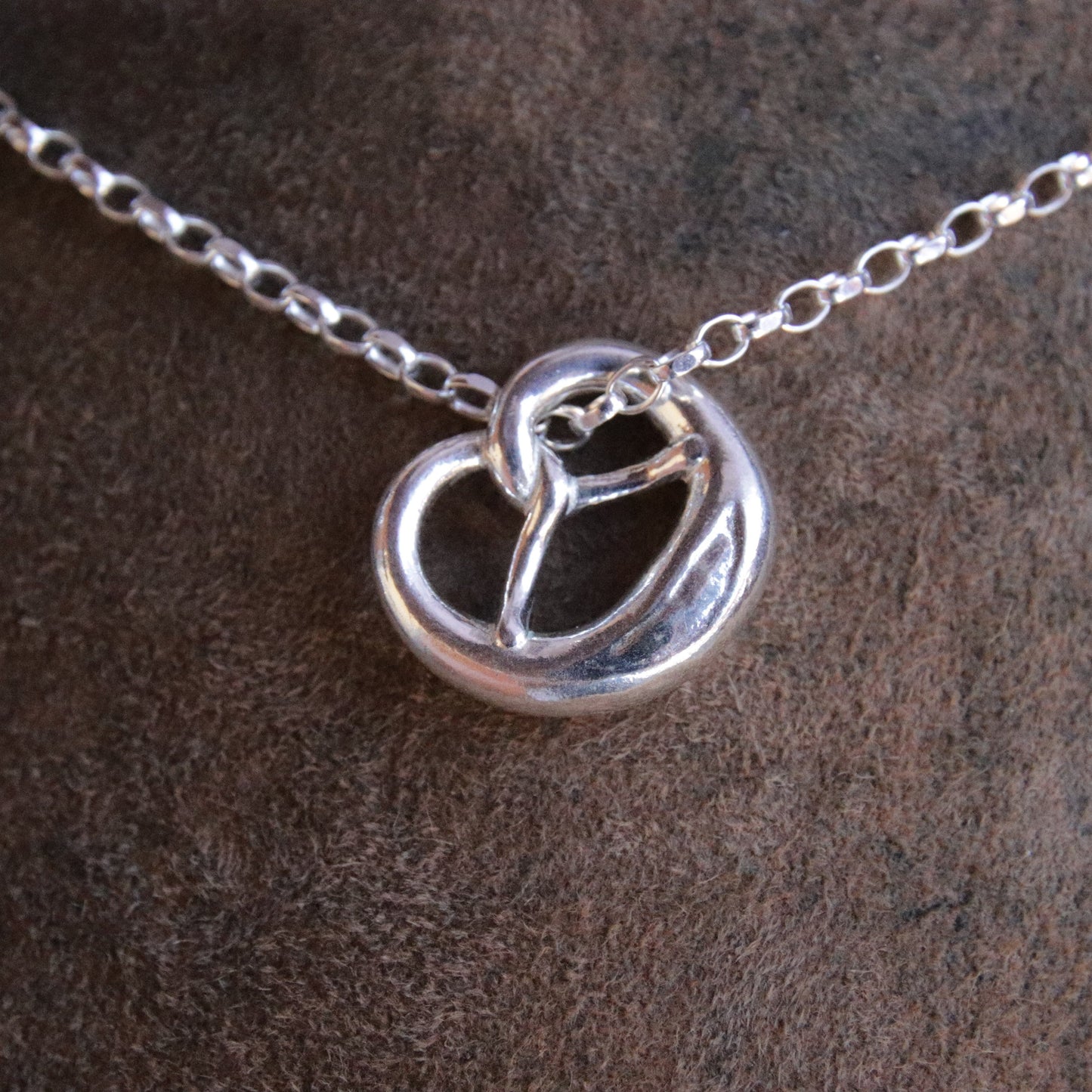 Brezn-Anhänger aus Argentium 940 Silber mit Silberkette auf Lederhosen-Leder
